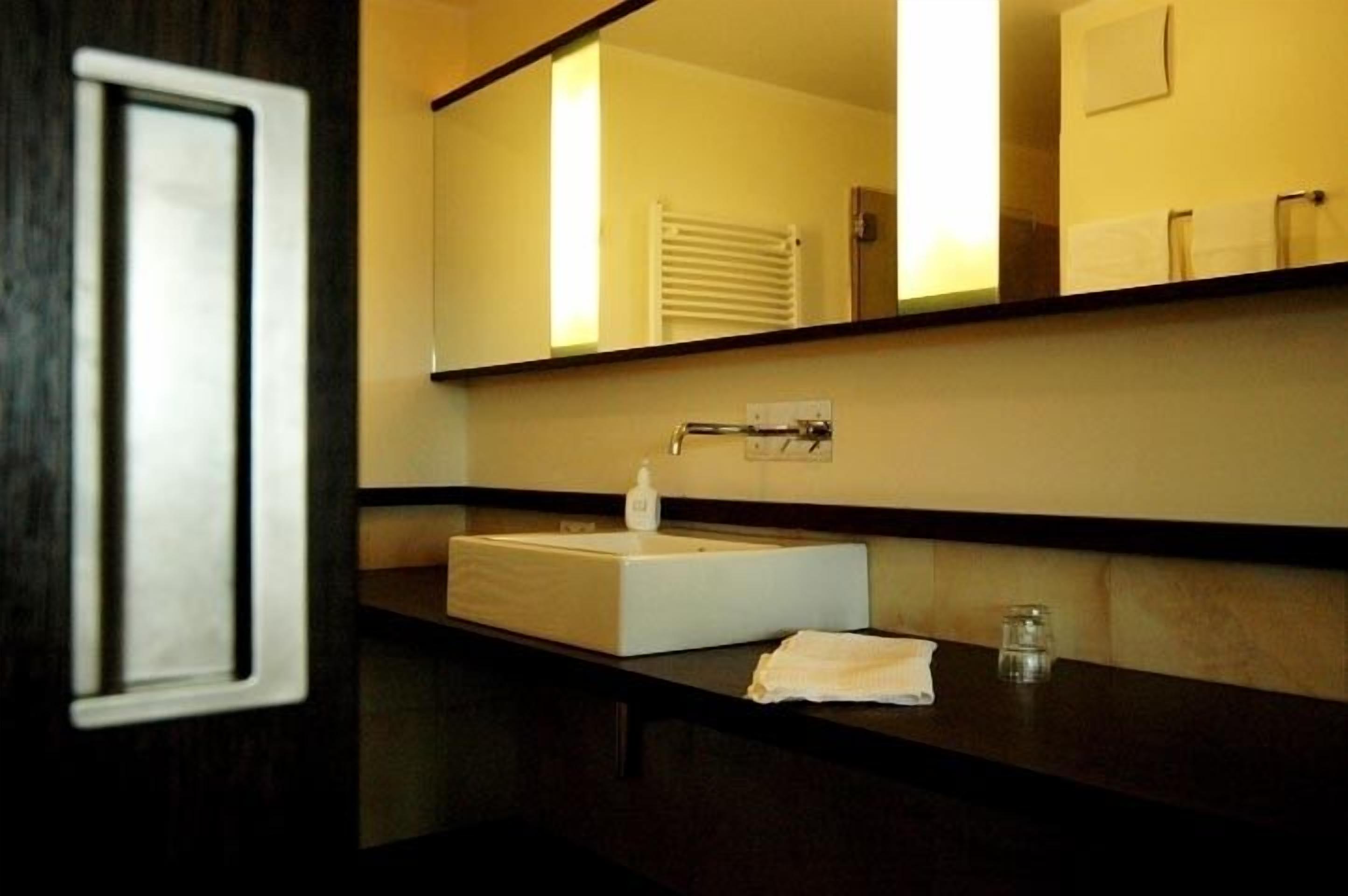 Un baño con un espejo grande, un lavabo, una toalla y un vaso de agua.