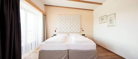 A bedroom with a bed, wooden beams, a window with curtains, and artwork on the wall.