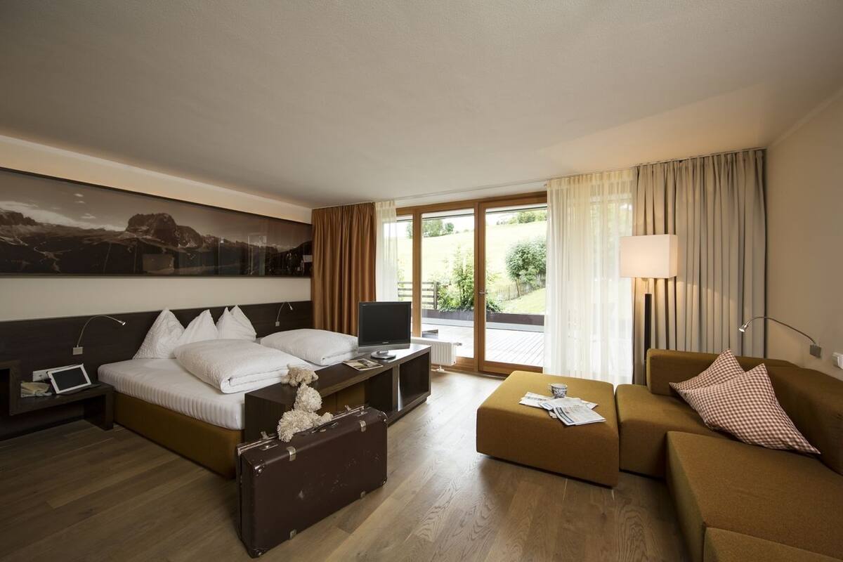 Ein Hotelzimmer mit Bett, Schreibtisch, Laptop, Koffer, Sofa und Lampe.