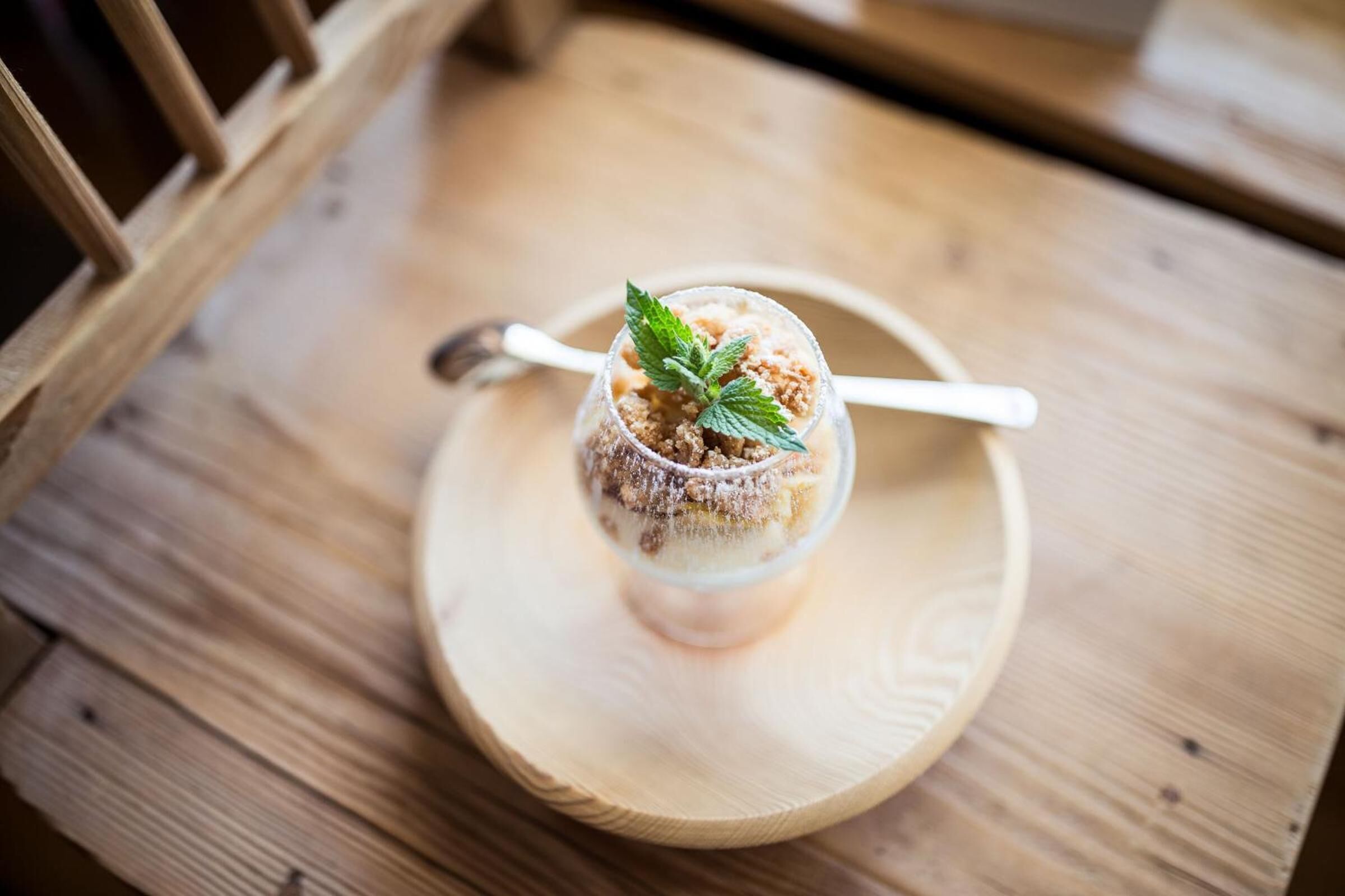A dessert in a clear glass cup on a wooden coaster.