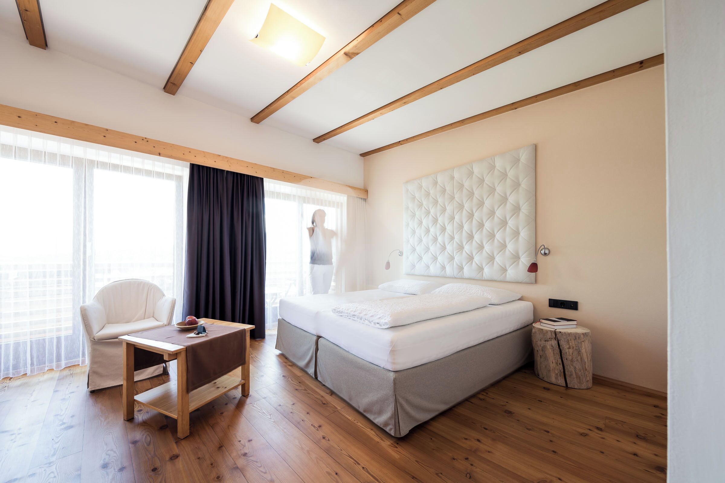 A bedroom with a bed, a desk, a chair, a window with curtains, and a wooden ceiling.