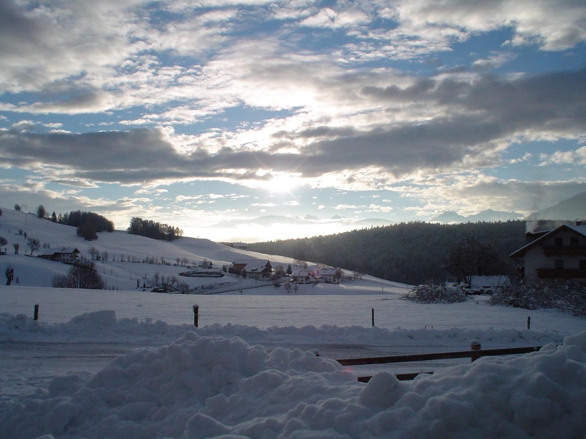 Paisaje nevado con una casa y una cerca en primer plano.
