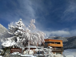 Un hotel moderno con un letrero que dice "Dolomitenblick alps boutique hotel", rodeado de árboles y montañas cubiertas de nieve.
