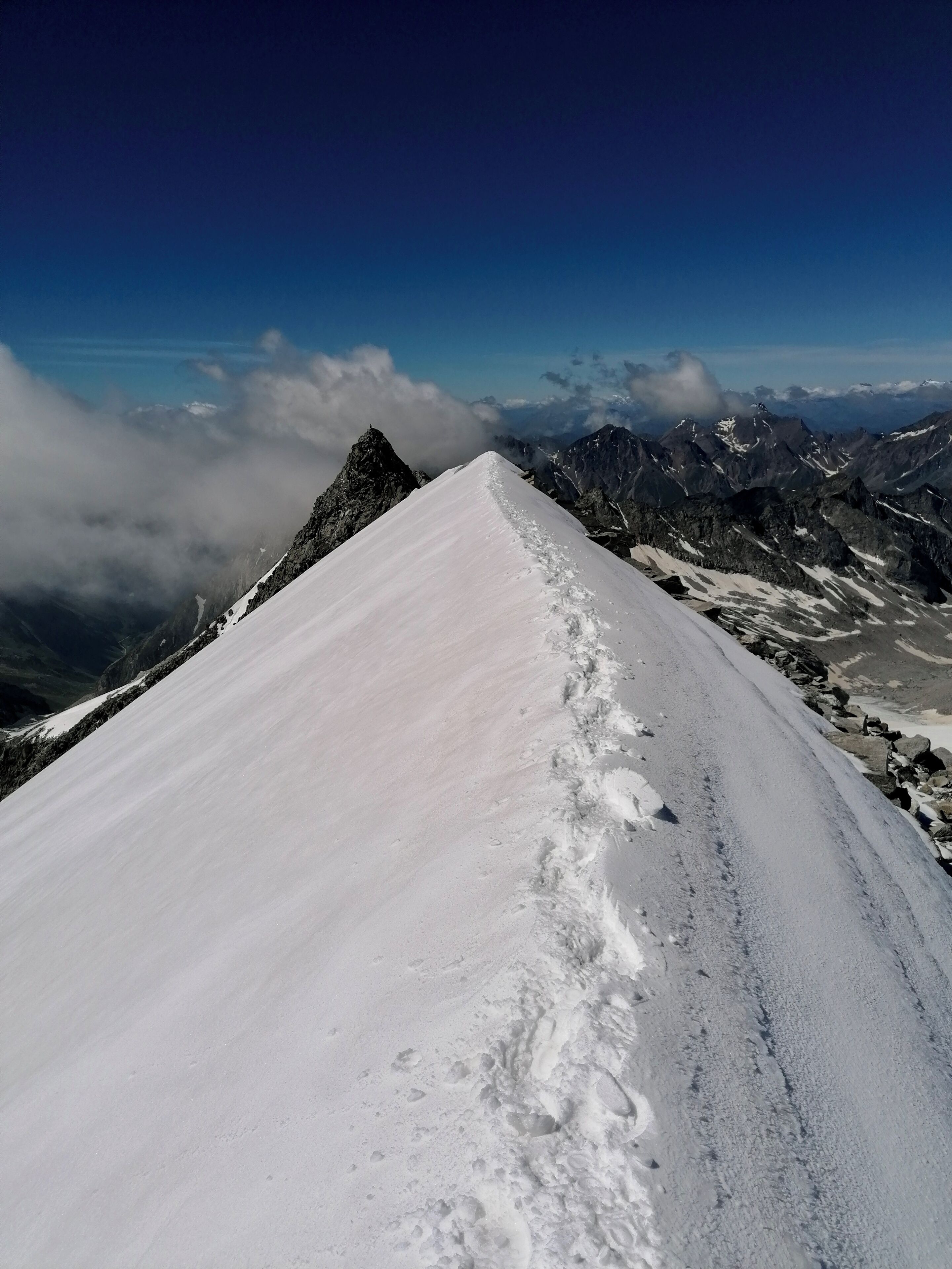 Camino nevado en la montaña, con terreno rocoso y cumbres lejanas.