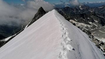 Camino nevado en la montaña, con terreno rocoso y cumbres lejanas.