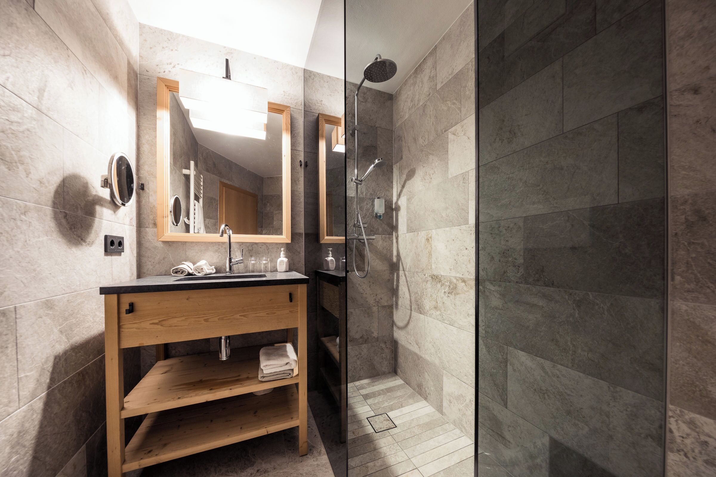 Un baño moderno con tocador de madera, cabina de ducha de vidrio y baldosas de mármol.