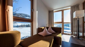 A cozy room with a sofa and a table, large windows with a view of snow-covered mountains. - Hotel Dolomitenblick (Terento)