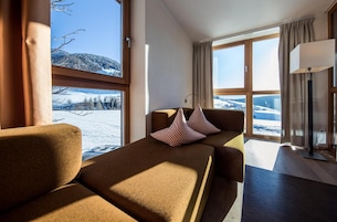 Una habitación acogedora con sofá y una mesa, ventanas amplias con vistas a montañas nevadas.