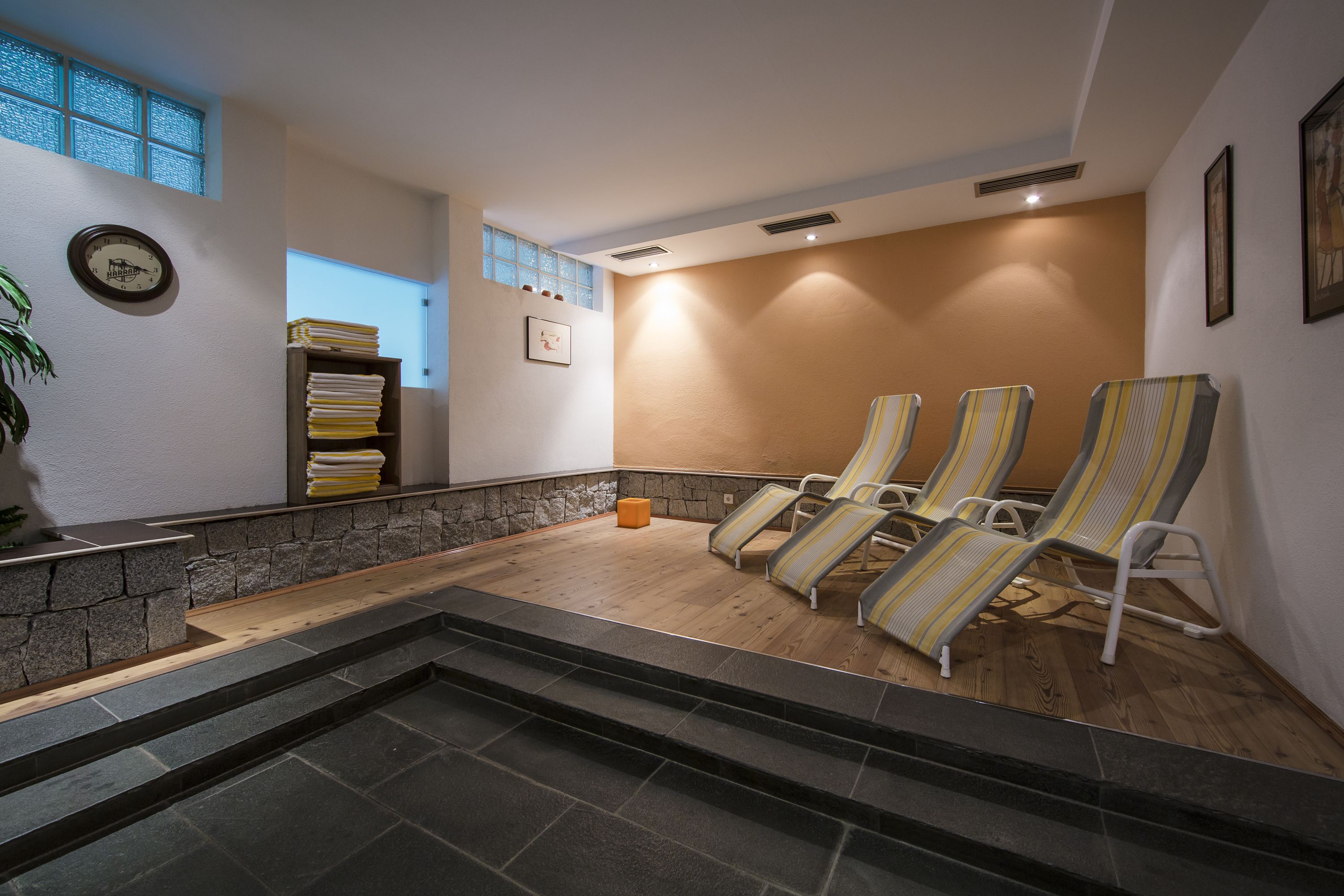 Zona de spa con pared de piedra, suelo de madera y tres sillones reclinables a rayas.