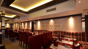 Un restaurante con asientos tapizados en rojo y mesas, iluminación ambiental y diseños decorativos en las paredes.