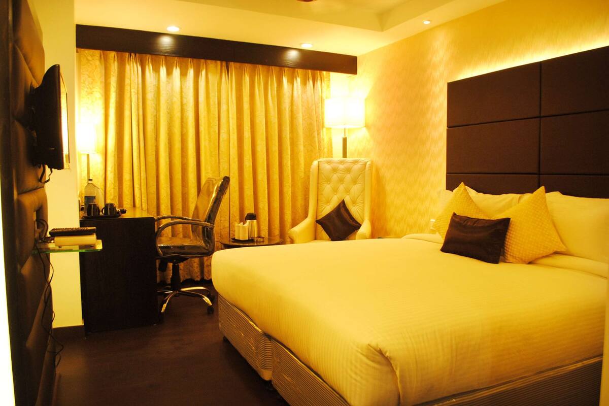 A hotel room with a large bed, a desk with a chair, a television, and a lamp.