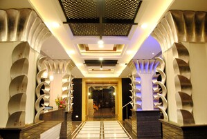 A hotel lobby with a modern design, featuring a central staircase, decorative columns, and a patterned ceiling.