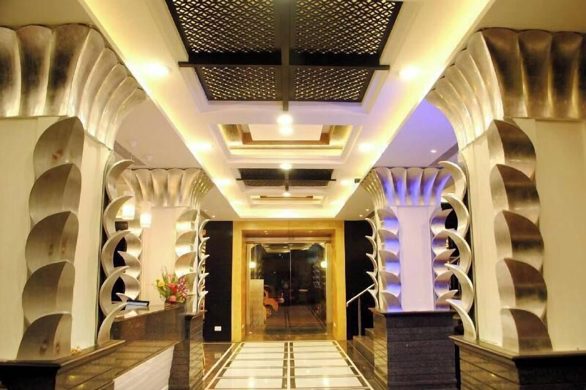 A hotel lobby with a modern design, featuring a central staircase, decorative columns, and a patterned floor.