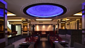 En moderne restaurant med et centralt spiseområde, siddebåse og et mønstret loft.