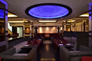 A modern restaurant with a central dining area, booths, and a patterned ceiling.