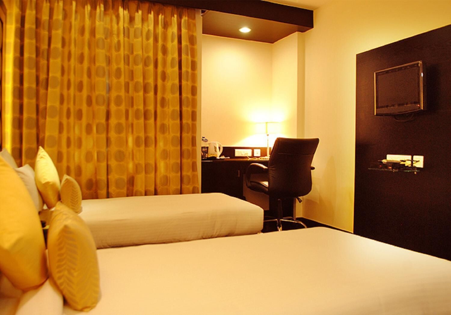 Habitación de hotel con dos camas, un escritorio con lámpara, una silla y un televisor en la pared.