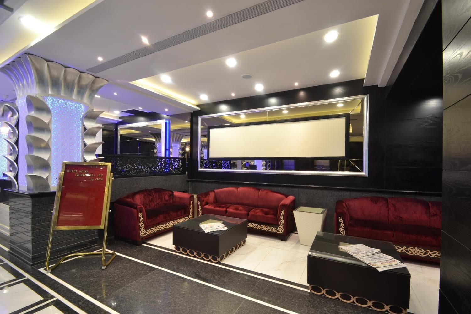 Un hall d’entrée moderne avec des canapés en velours rouge, un comptoir d’accueil et un grand écran.
