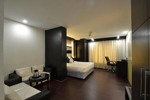 A hotel room with a bed, a desk, a chair, a coffee table, and a TV.