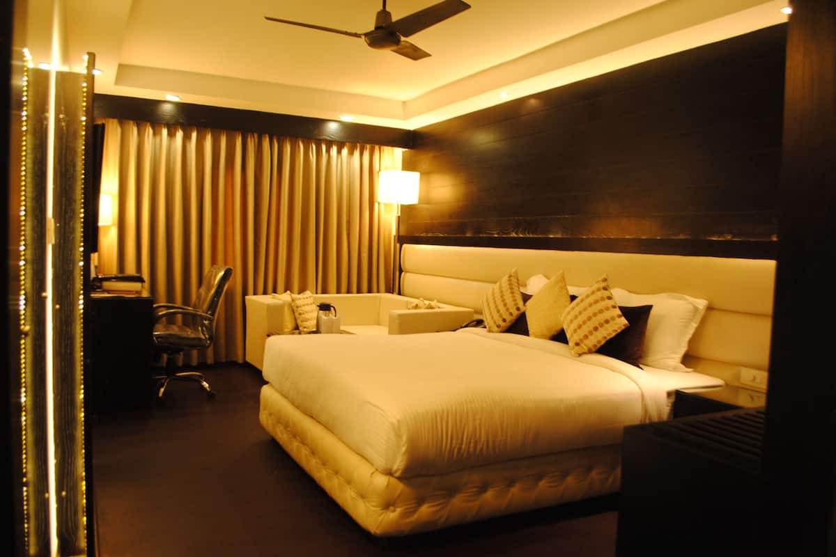 A hotel room with a large bed, a desk, a chair, and a ceiling fan.