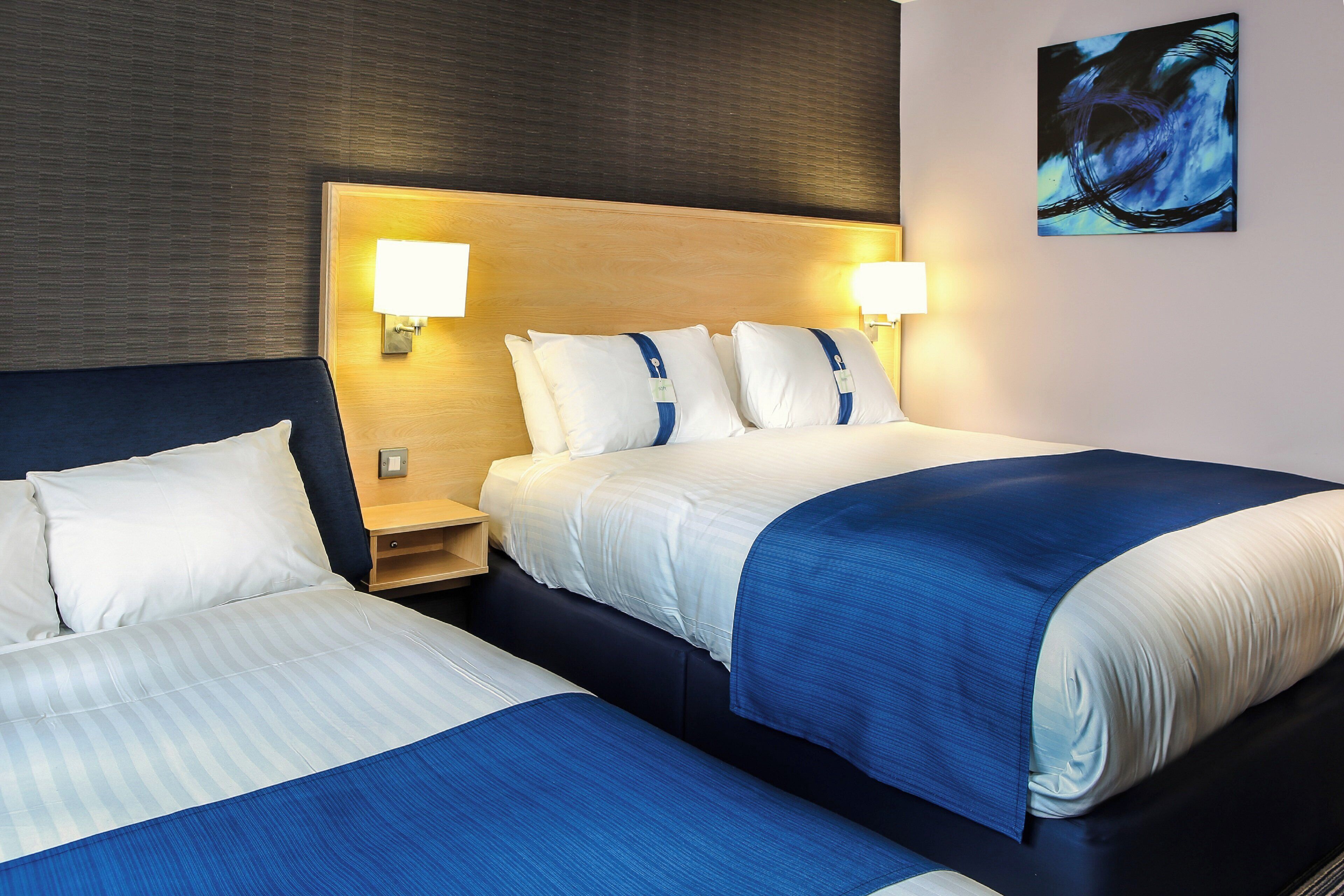 Habitación de hotel con dos camas, cada una con cabecero, lámparas de noche y mesitas de noche.