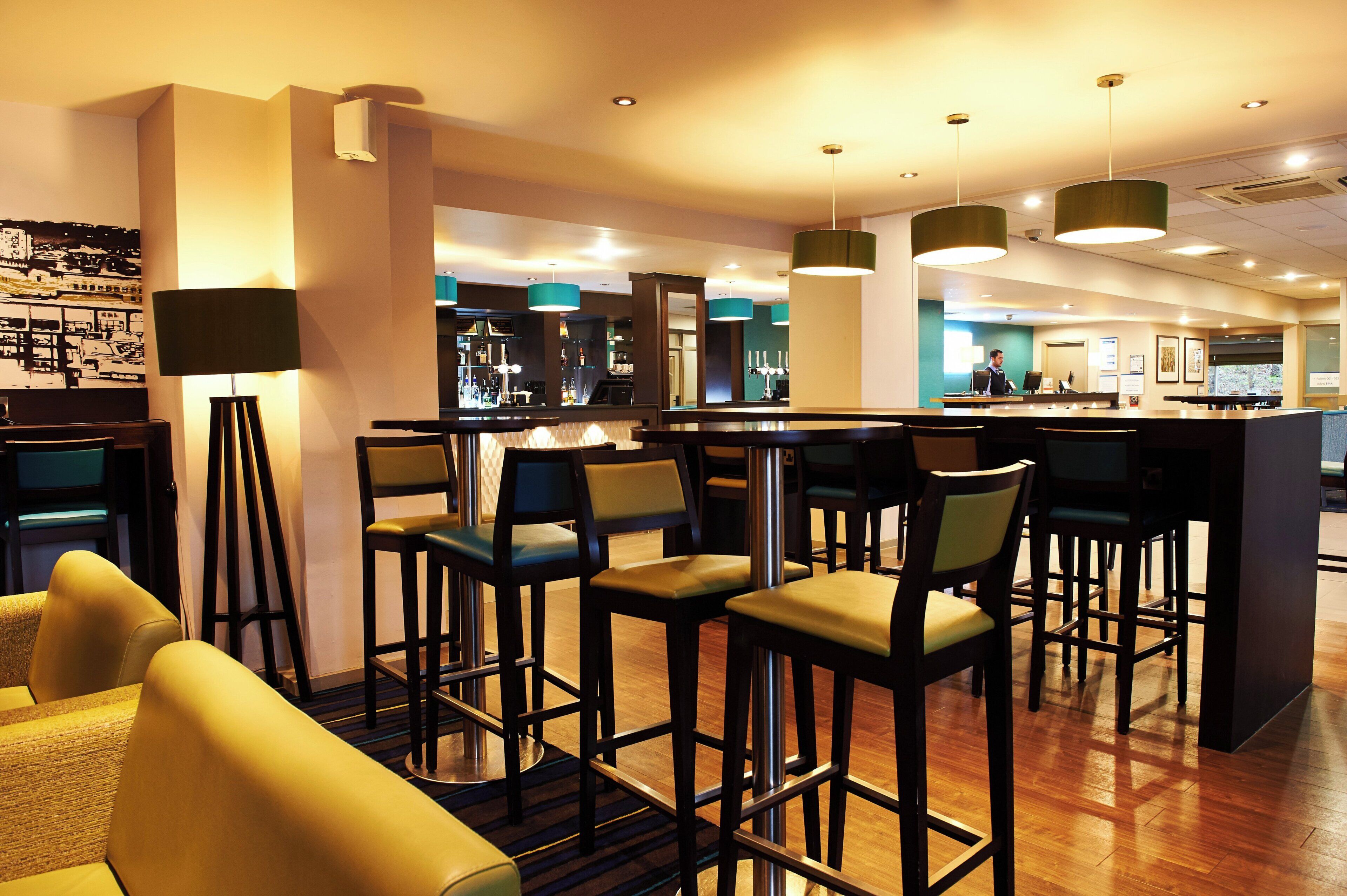 A bar area with high stools, a bar counter, and pendant lighting.