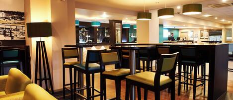 A bar area with high stools, a bar counter, and pendant lighting.