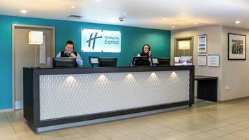 A reception desk with a Holiday Inn Express sign, two receptionists, and a modern interior with a teal accent wall.