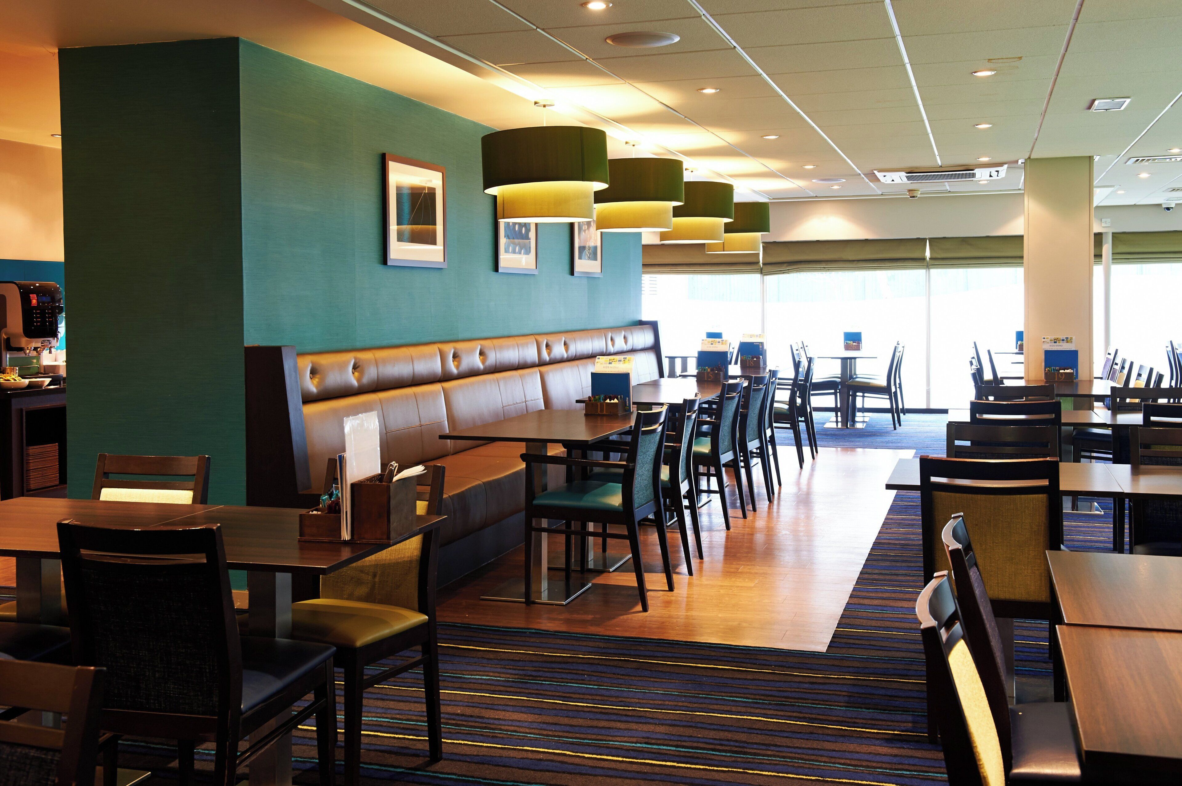 A restaurant with booths, tables, and chairs, featuring a striped carpet and pendant lighting.