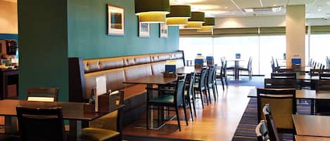 A restaurant with booths, tables, and chairs, featuring a striped carpet and pendant lighting.