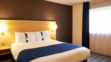 Habitación de hotel con una cama grande, dos lámparas de noche, cabecero de madera y una ventana con cortinas.