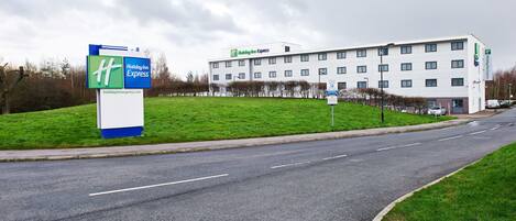 A Holiday Inn Express hotel with a large sign, a parking lot, and a grassy area in front.