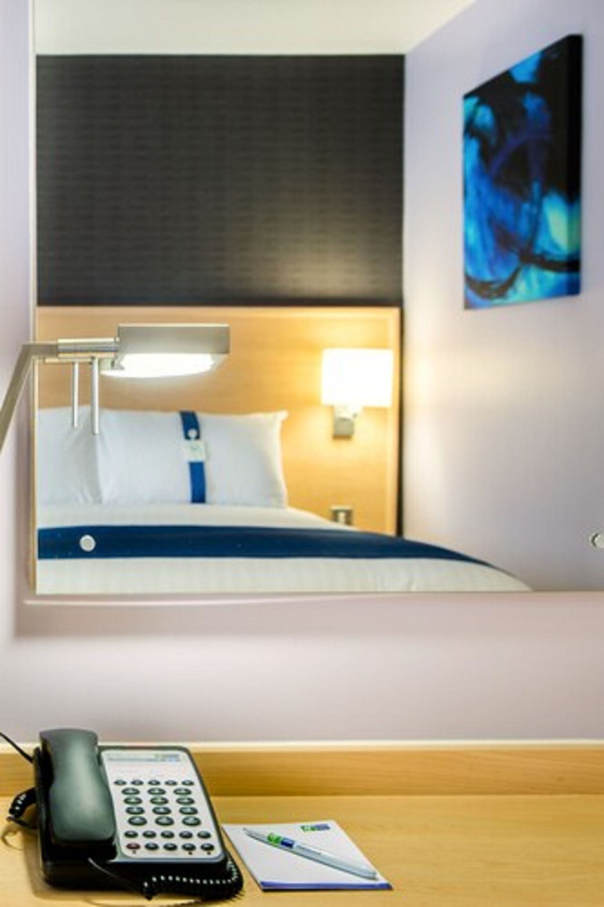 A hotel room with a bed, a desk with a telephone, a lamp, and a painting on the wall.