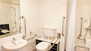 Un baño con lavamanos, inodoro y zona de ducha, equipado con barras de apoyo y pasamanos.