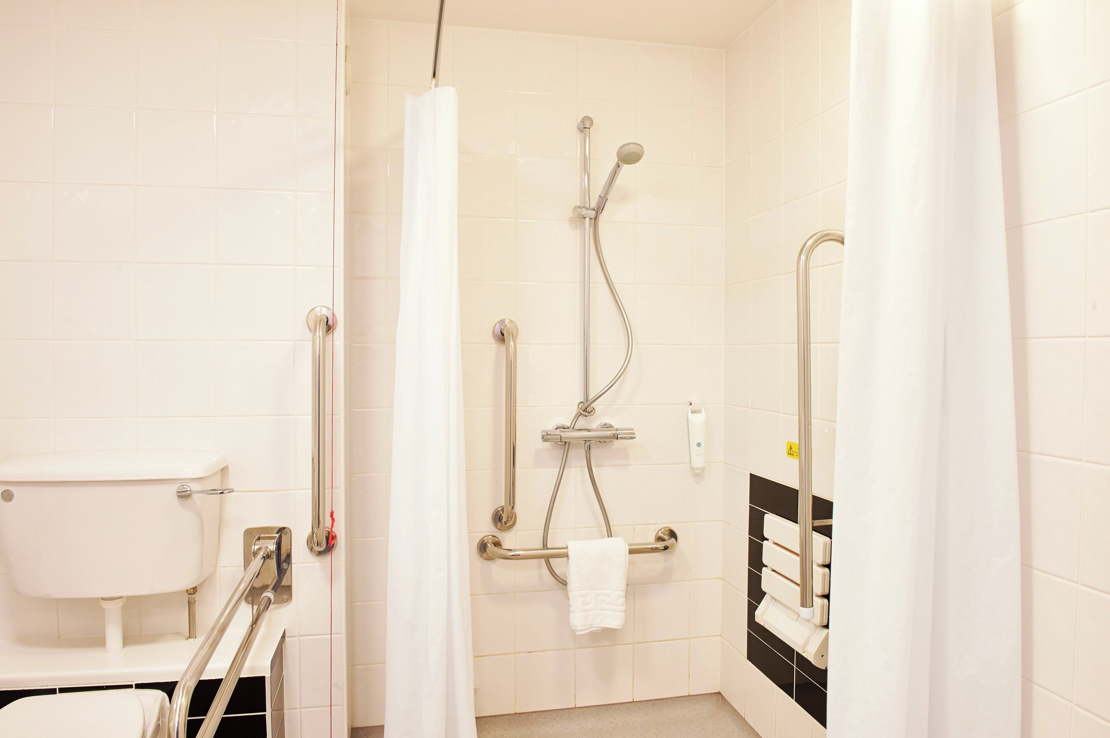 Een moderne badkamer met een inloopdouche, handgrepen, een toilet met een veiligheidsbeugel en een handdoekhouder.