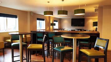 Een restaurant met meerdere tafels en stoelen, een bar en een televisiescherm aan de muur.