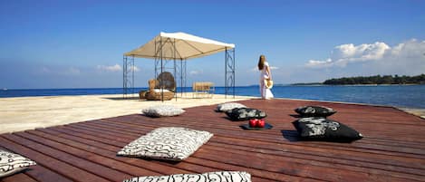 Una terraza de madera con sillones de descanso y un dosel, con vista a una playa.