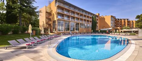 Un hôtel doté d’une grande piscine, de chaises longues et d’un jardin bien entretenu.