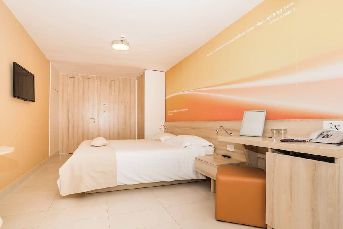 Une chambre d’hôtel équipée d’un lit, d’un bureau et d’un téléviseur fixé au mur.