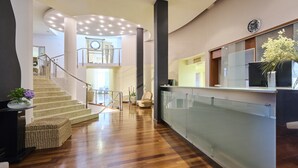 Un moderno vestíbulo de hotel con piso de madera, una escalera, mostrador de recepción y un reloj grande en la pared.
