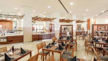 Un restaurante moderno con mesas y sillas de madera, una barra central con vitrina y un interior luminoso y bien iluminado.