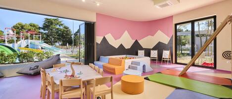 A children's play area with colorful mats, a table with chairs, and a wall with a mountain design.