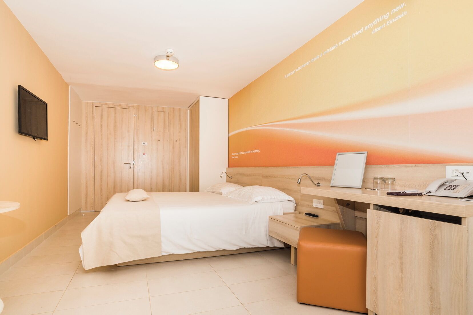 Ein Hotelzimmer mit Bett, Schreibtisch und einem an der Wand befestigten Fernseher.
