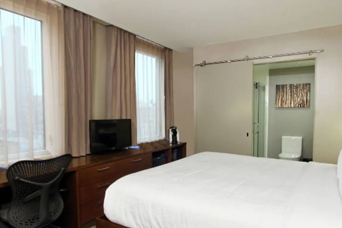 Habitación de hotel con cama, escritorio con televisor, una silla, armario y baño con inodoro.