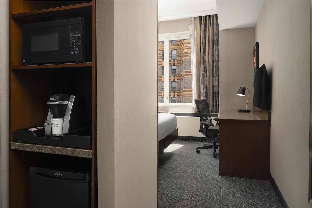 Habitación de hotel con kitchenette, cama, escritorio y televisor.