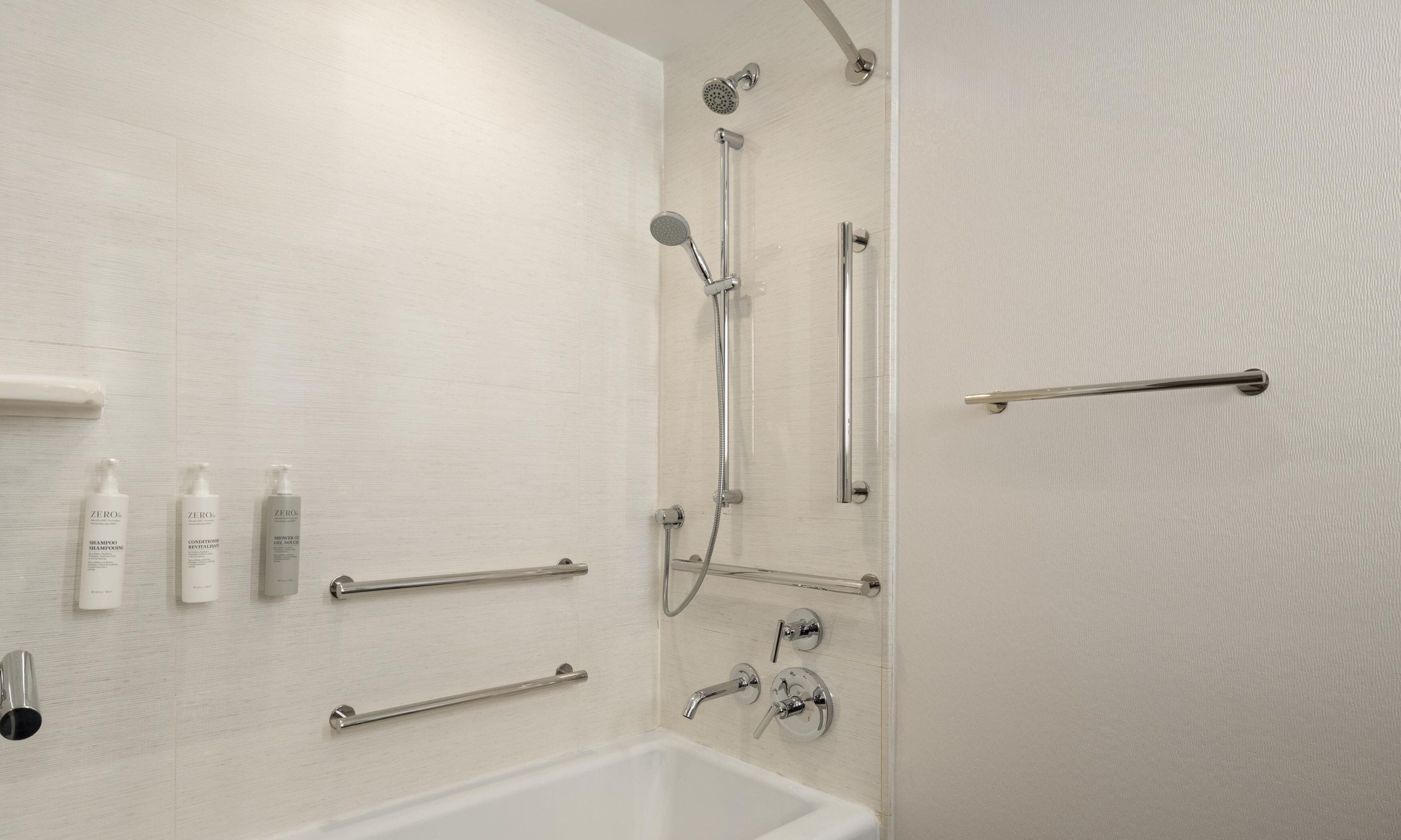 Une salle de bain équipée d’une douche, de barres d’appui et d’un lavabo.