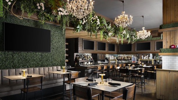 Un restaurante con zona de bar, mesas y sillas de madera, y una pared verde con plantas.