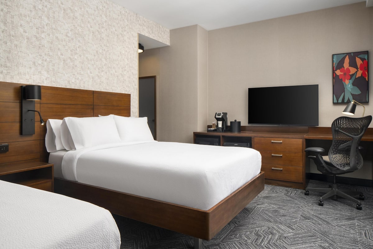 Habitación de hotel con una cama grande, un escritorio con computadora, televisor y cafetera.