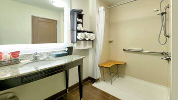 A bathroom with a sink, mirror, towel rack, shower, and a small wooden stool.