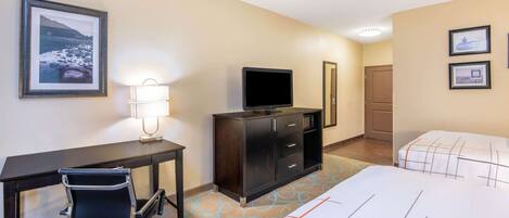A hotel room with a desk, chair, television, dresser, two beds, and framed pictures on the walls.