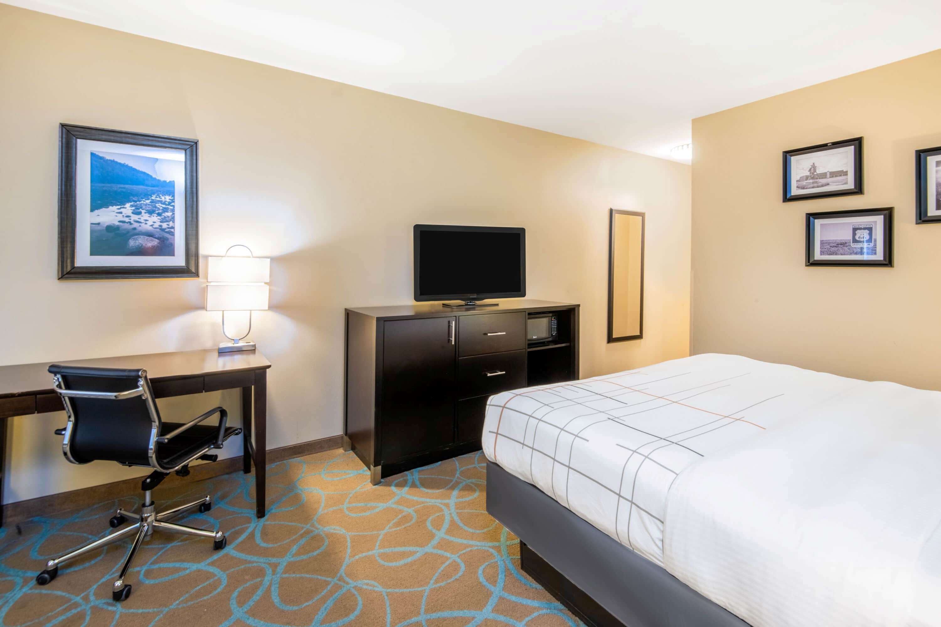A hotel room with a bed, desk, chair, TV, and framed pictures on the wall.